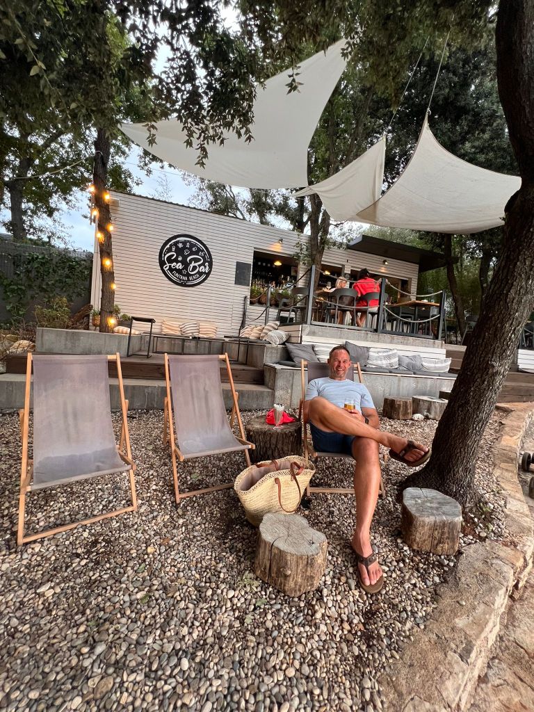 Man relaxing at a bar watching the sunset on a pebble beach near Porec Croatia.