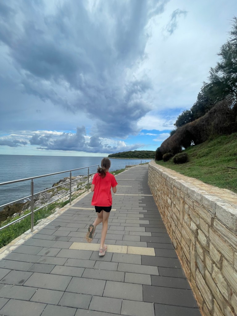 Active Family Holiday Croatia at Valamar Istra Camping. Girl Running along the sea front on holiday.